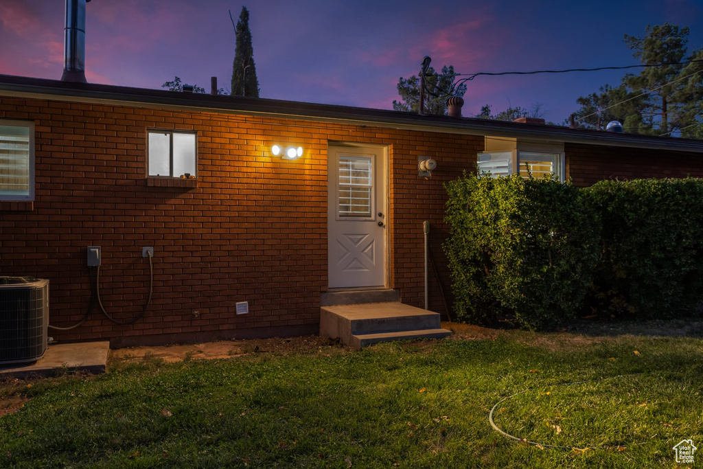 Exterior entry at dusk with central air condition unit and a lawn