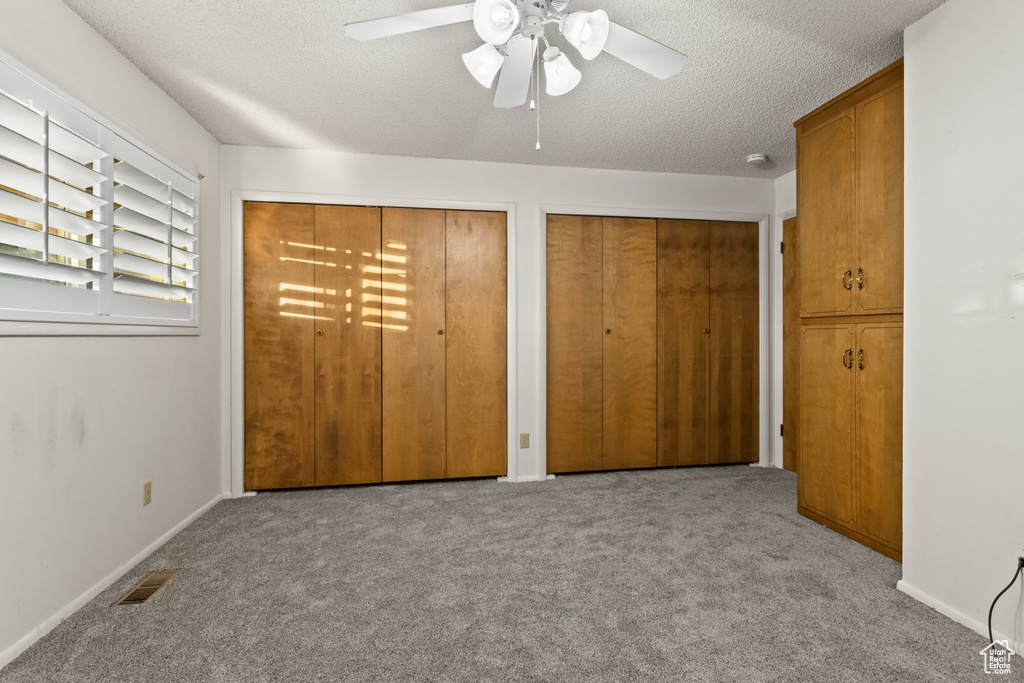 Unfurnished bedroom with light carpet, ceiling fan, multiple closets, and a textured ceiling