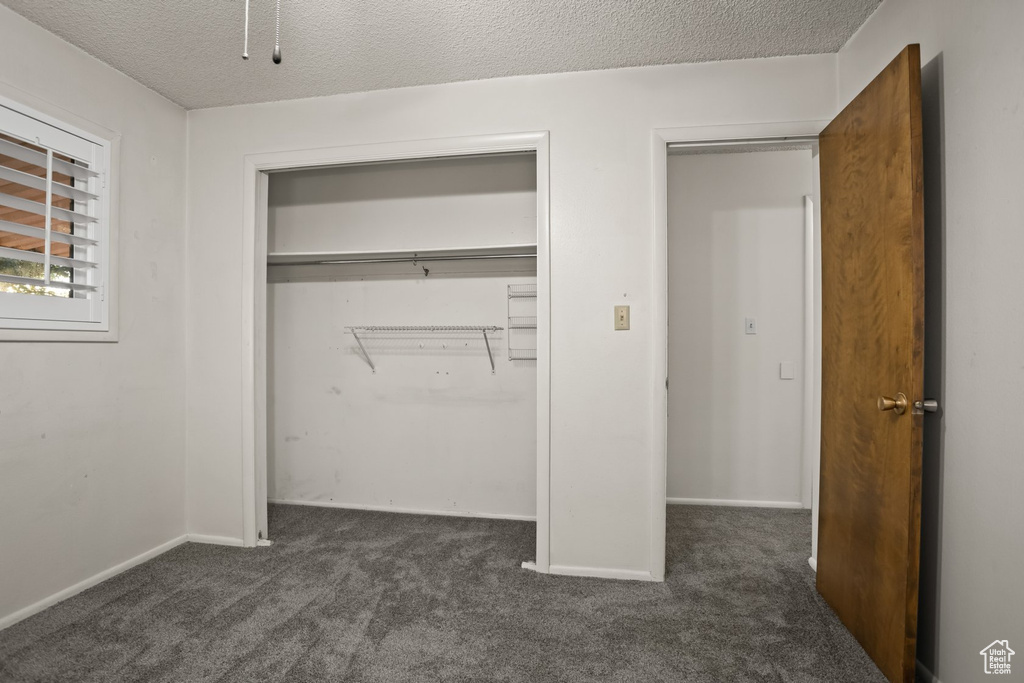 Unfurnished bedroom featuring a closet, dark carpet, and a textured ceiling