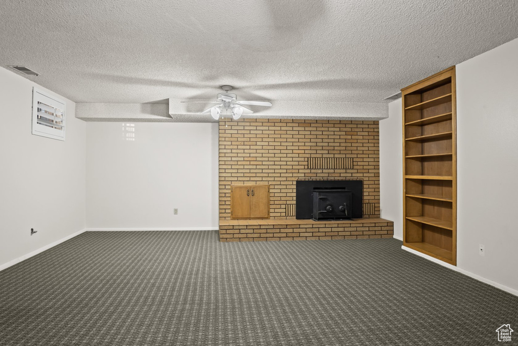 Basement featuring ceiling fan, a textured ceiling, dark colored carpet, and a wood stove