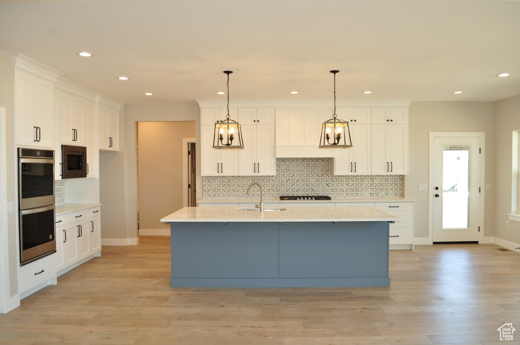 Kitchen featuring pendant lighting, a kitchen island with sink, light hardwood / wood-style flooring, and white cabinetry