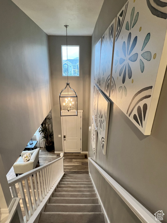 Staircase with hardwood / wood-style floors and an inviting chandelier