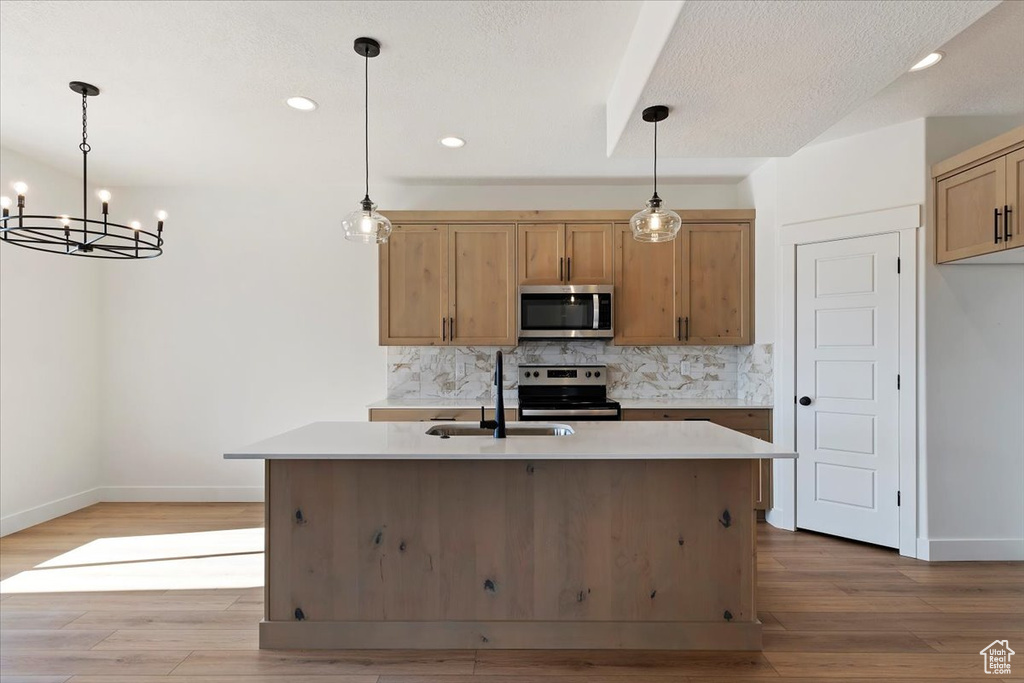 Kitchen featuring appliances with stainless steel finishes, hanging light fixtures, a center island with sink, and light hardwood / wood-style flooring