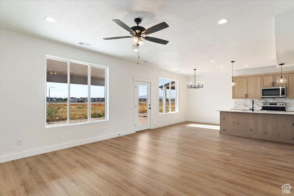 Unfurnished living room with ceiling fan with notable chandelier, light wood-type flooring, sink, and a healthy amount of sunlight