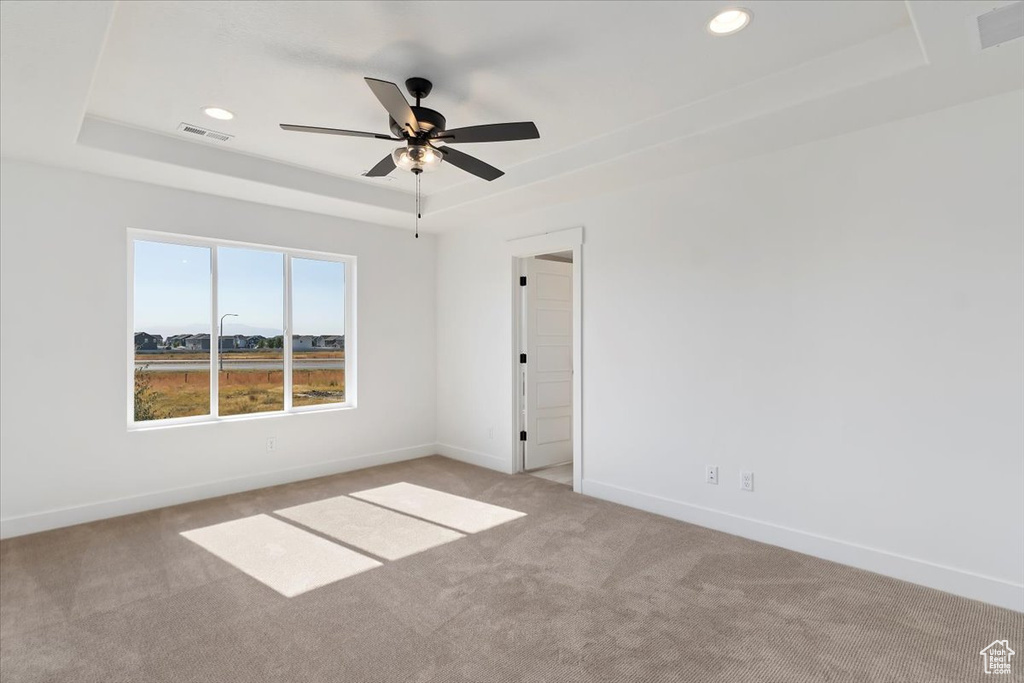 Unfurnished room with a raised ceiling, light colored carpet, and ceiling fan