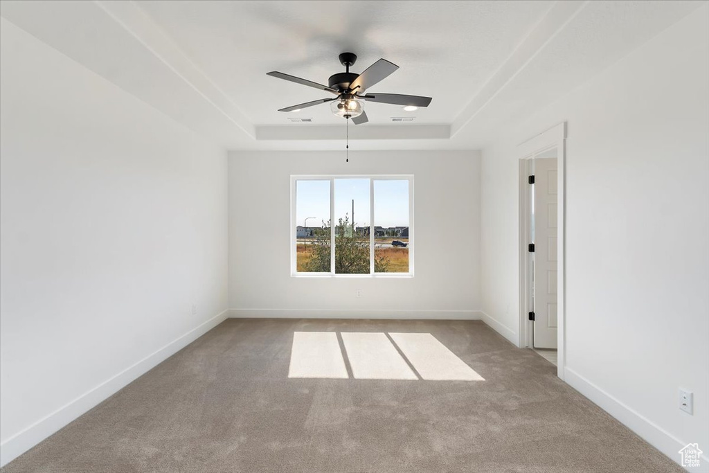 Empty room featuring ceiling fan, a tray ceiling, and light colored carpet