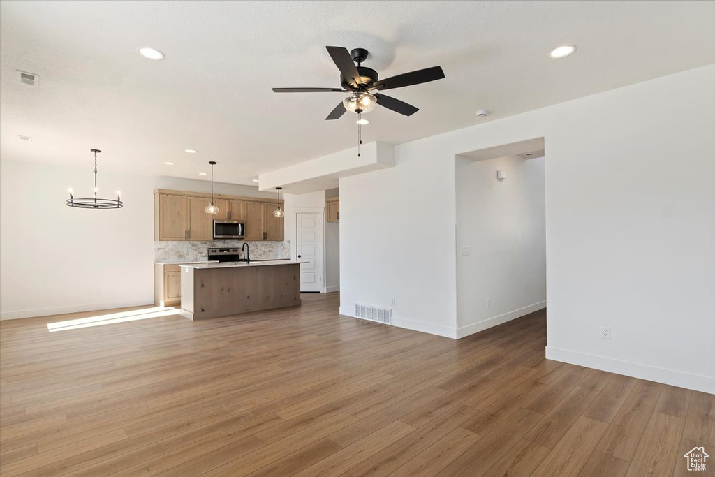 Unfurnished living room featuring ceiling fan with notable chandelier and hardwood / wood-style flooring