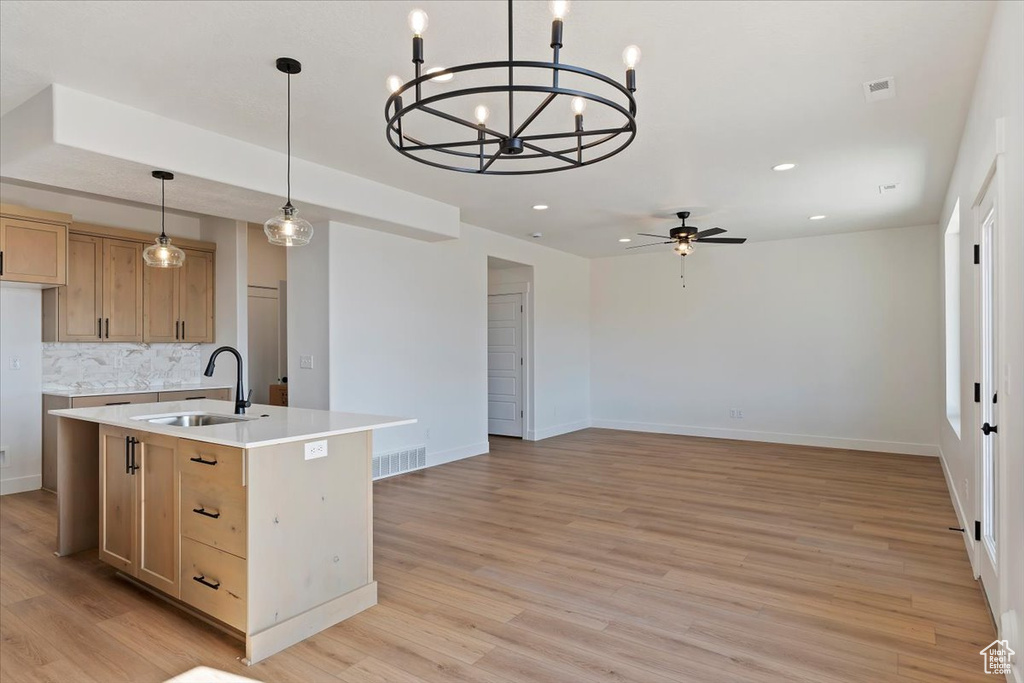 Kitchen featuring an island with sink, pendant lighting, sink, and light wood-type flooring