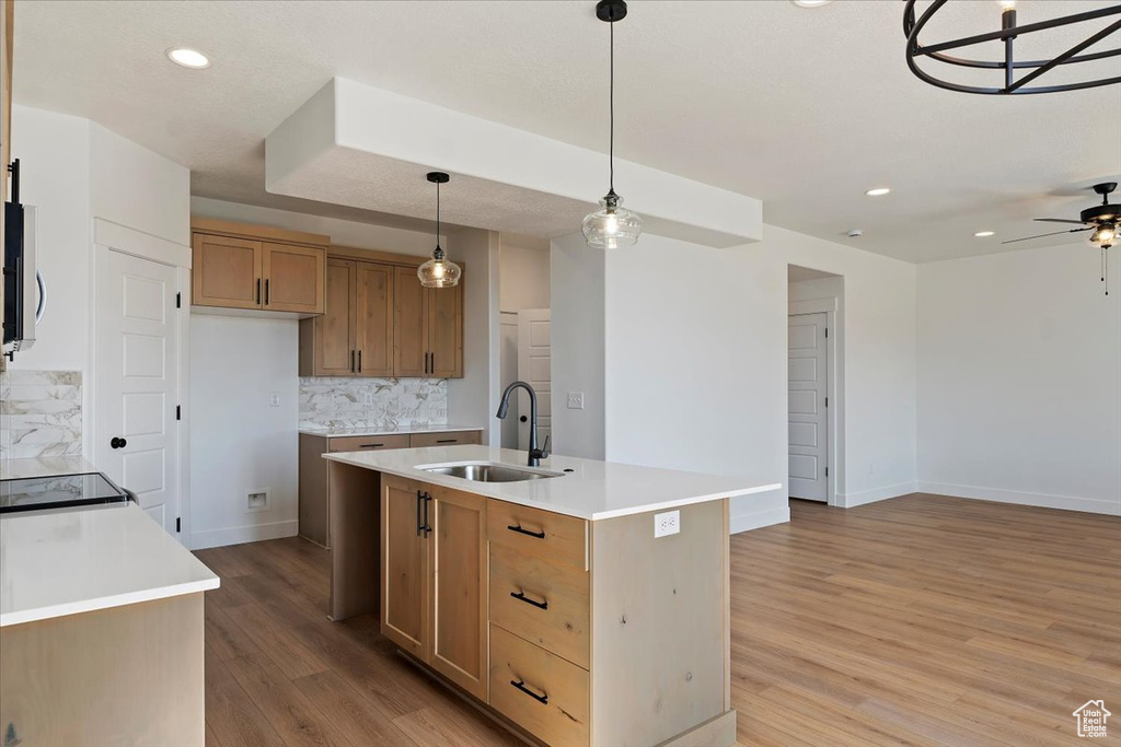 Kitchen with hanging light fixtures, sink, a kitchen island with sink, backsplash, and light hardwood / wood-style flooring