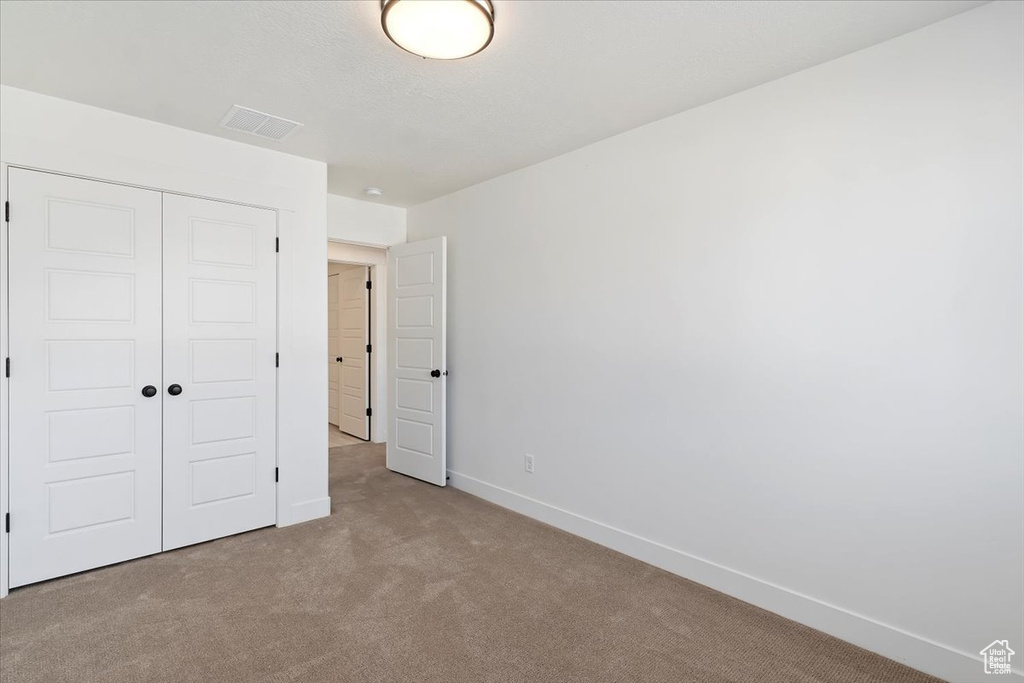 Unfurnished bedroom with light carpet and a closet