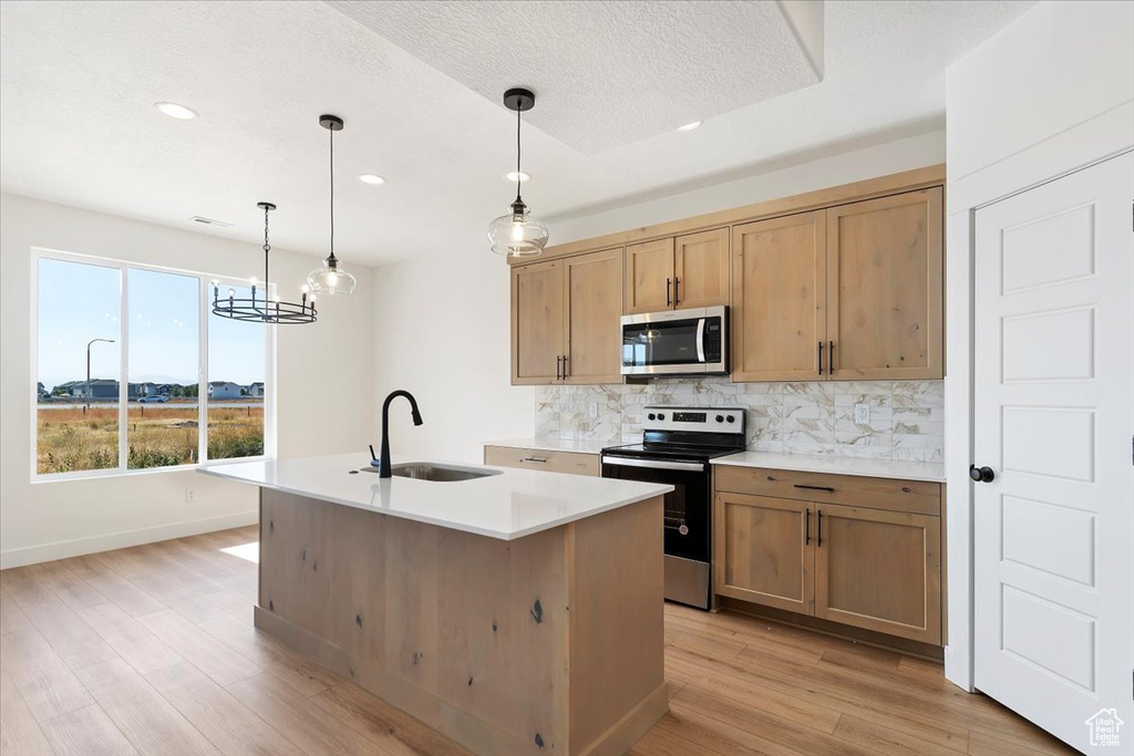 Kitchen with hanging light fixtures, sink, a kitchen island with sink, light hardwood / wood-style flooring, and appliances with stainless steel finishes