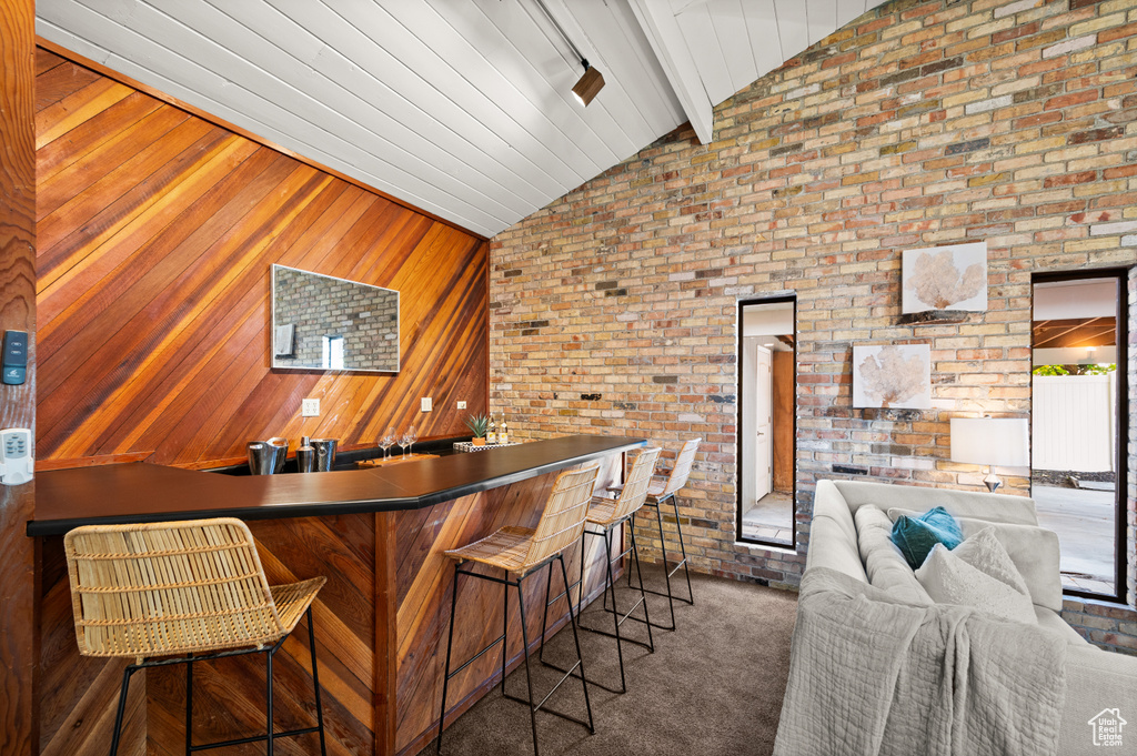 Bar with brick wall, wooden walls, lofted ceiling with beams, and dark colored carpet