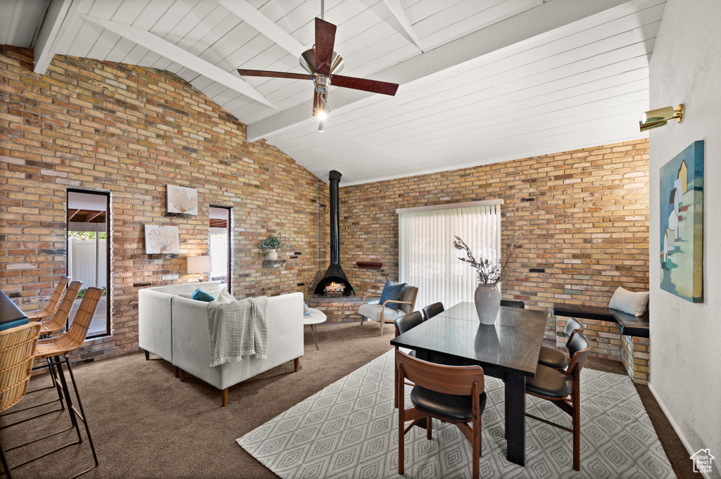 Carpeted living room with a wood stove, beamed ceiling, and brick wall