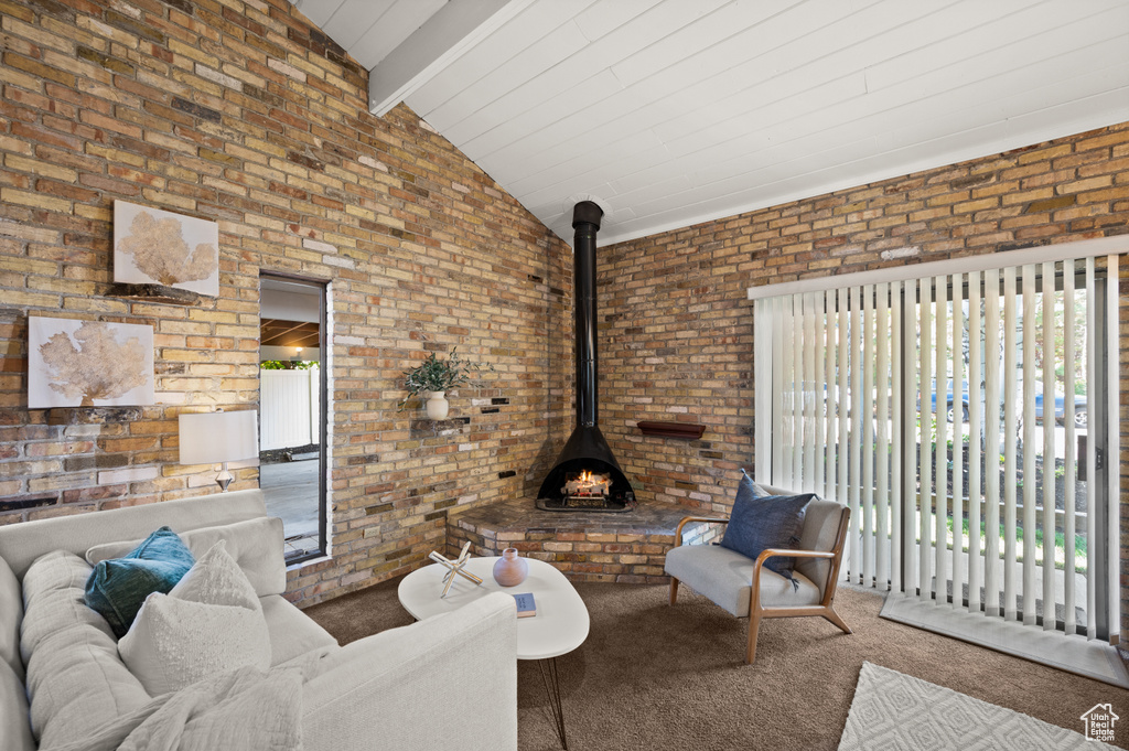 Carpeted living room featuring brick wall, vaulted ceiling with beams, and a wood stove