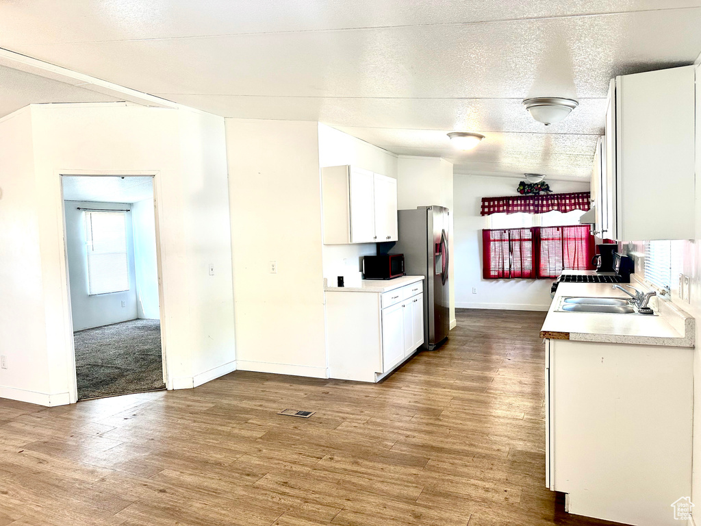 Kitchen with sink, a textured ceiling, white cabinetry, stainless steel refrigerator with ice dispenser, and light wood-type flooring