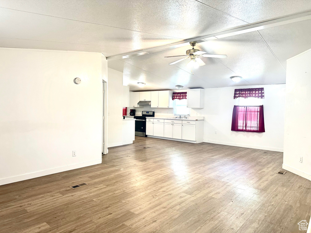 Unfurnished living room featuring lofted ceiling, ceiling fan, light hardwood / wood-style floors, and a textured ceiling