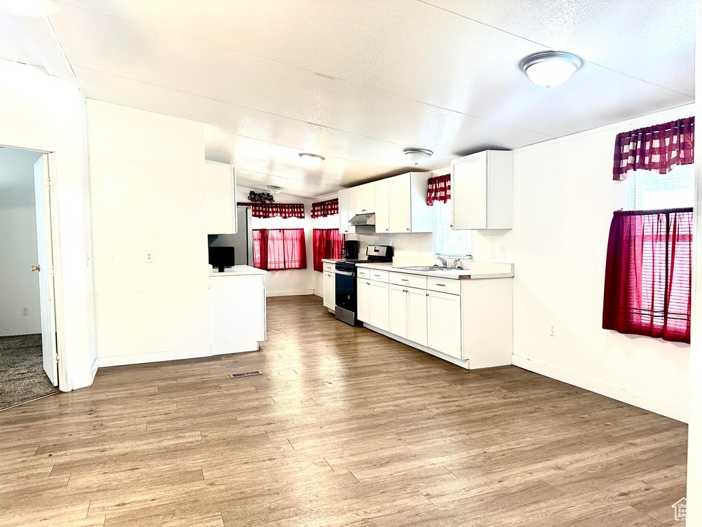 Kitchen featuring stainless steel range, sink, light hardwood / wood-style floors, and white cabinetry