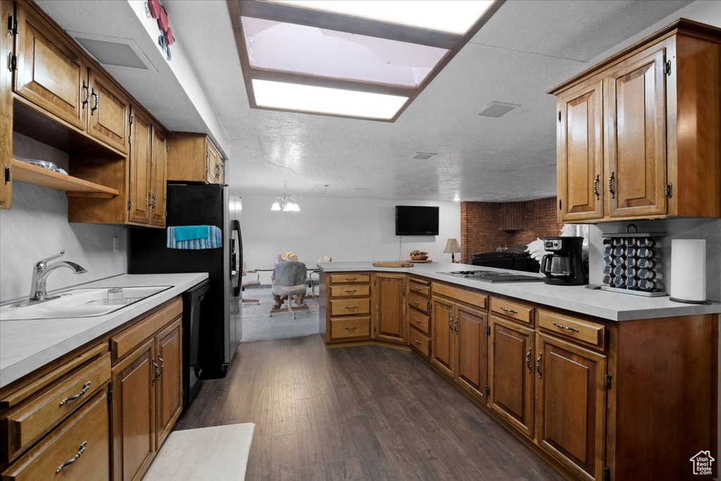 Kitchen with dark wood-type flooring, a notable chandelier, sink, black appliances, and a textured ceiling