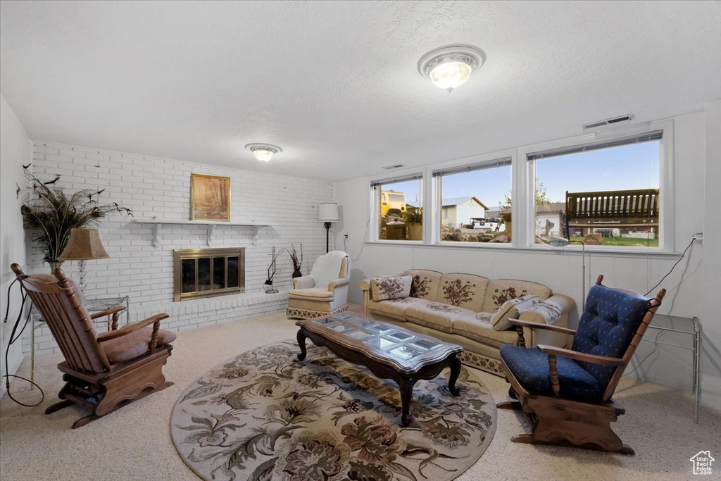 Living room with a brick fireplace, brick wall, a textured ceiling, and carpet flooring