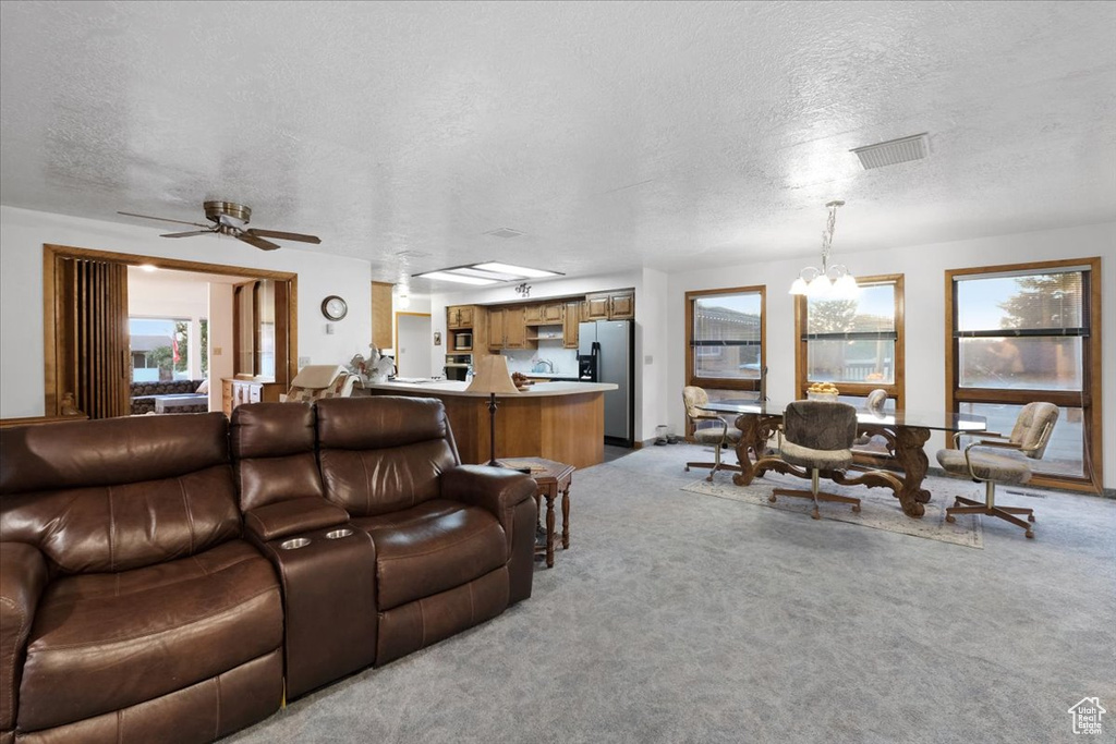 Carpeted living room featuring ceiling fan with notable chandelier and a textured ceiling