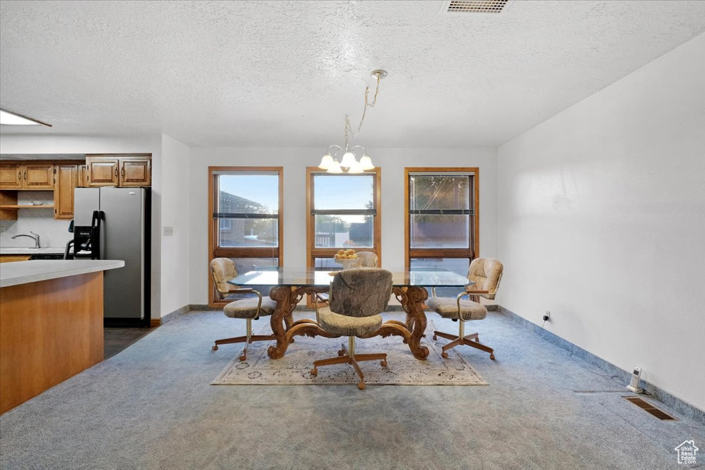 Carpeted dining room featuring sink, an inviting chandelier, and a textured ceiling