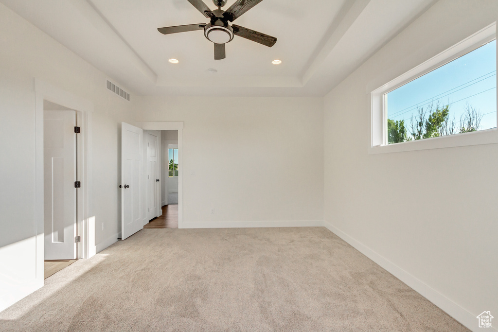 Carpeted spare room with a tray ceiling and ceiling fan