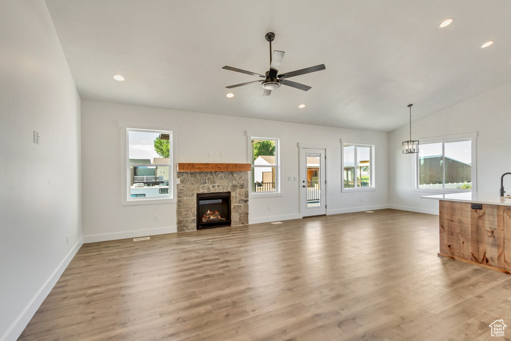 Unfurnished living room featuring plenty of natural light, a stone fireplace, vaulted ceiling, and wood-type flooring