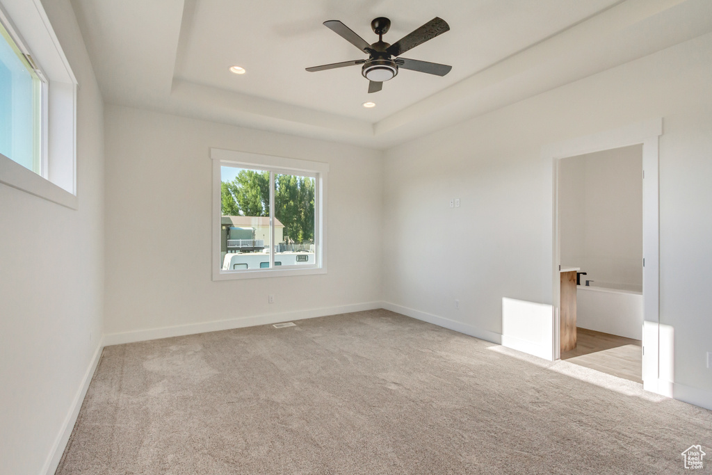 Spare room featuring light colored carpet, ceiling fan, and a raised ceiling