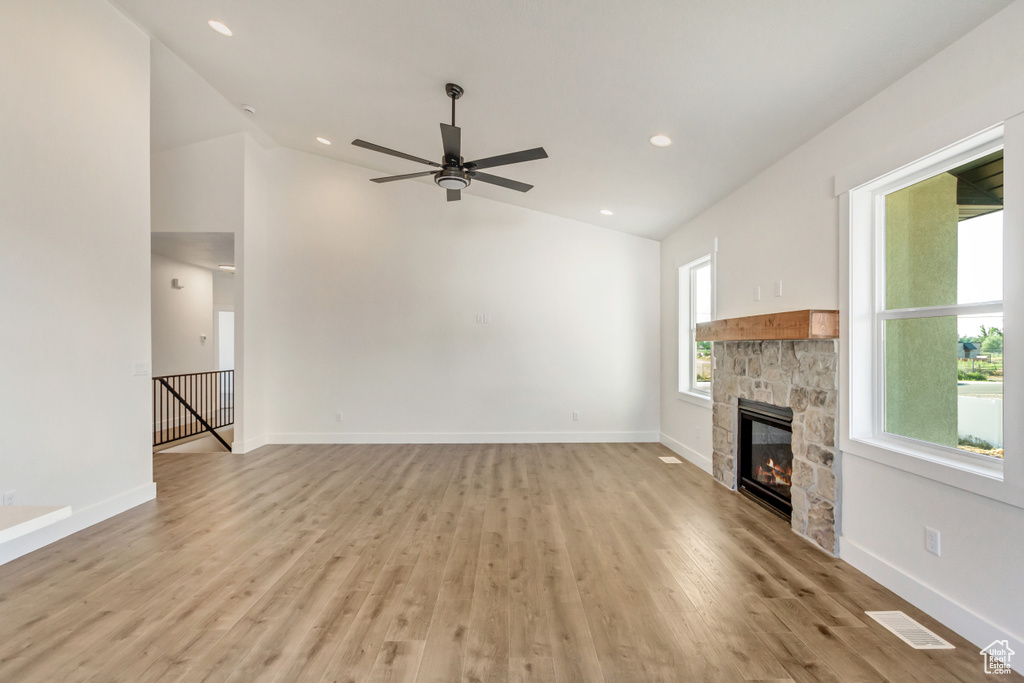 Unfurnished living room with ceiling fan, a stone fireplace, vaulted ceiling, and light hardwood / wood-style flooring