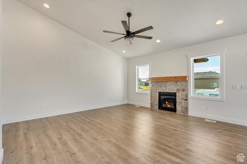 Unfurnished living room with lofted ceiling, ceiling fan, light wood-type flooring, and a stone fireplace