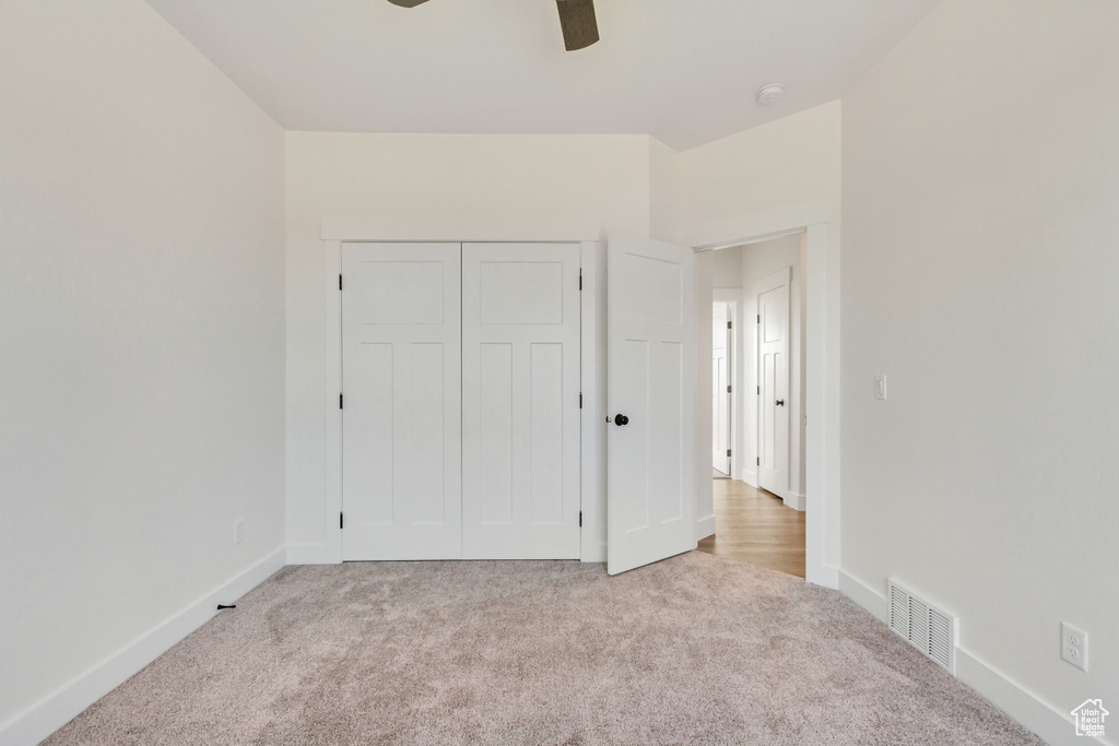 Unfurnished bedroom featuring ceiling fan, a closet, and light colored carpet