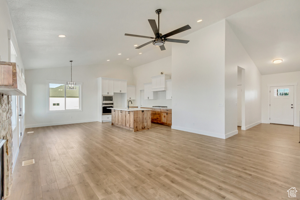 Unfurnished living room with ceiling fan with notable chandelier, light hardwood / wood-style floors, high vaulted ceiling, and sink