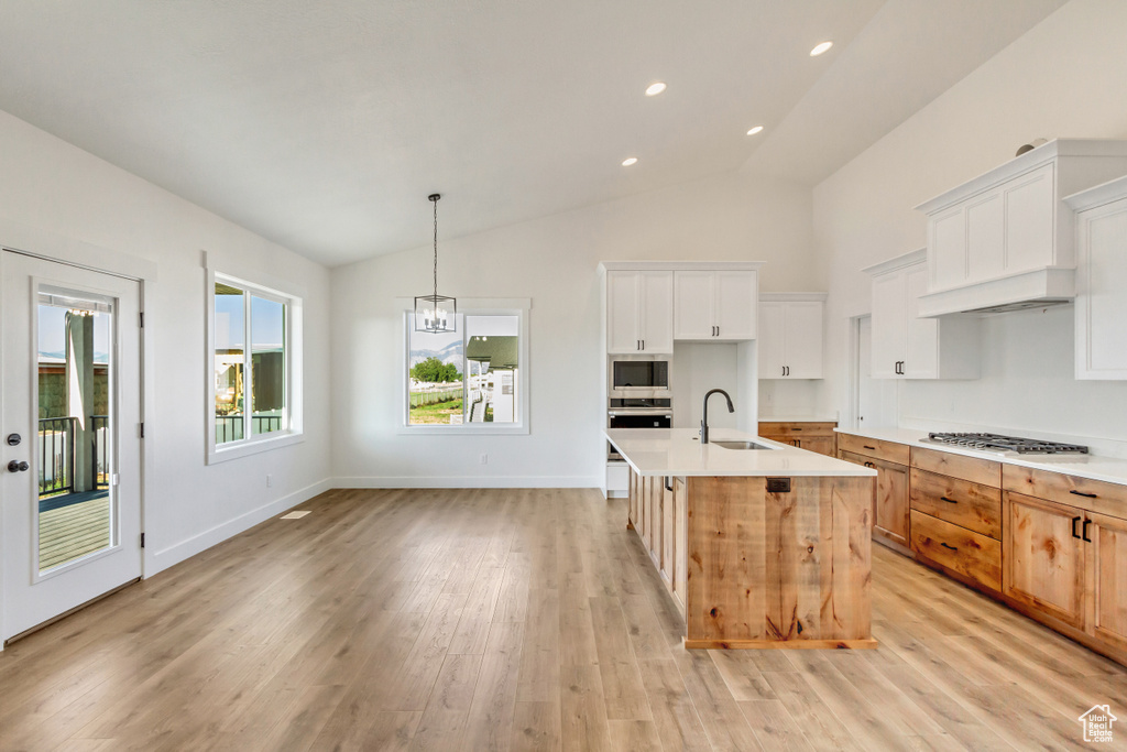 Kitchen featuring vaulted ceiling, white cabinetry, decorative light fixtures, and a kitchen island with sink