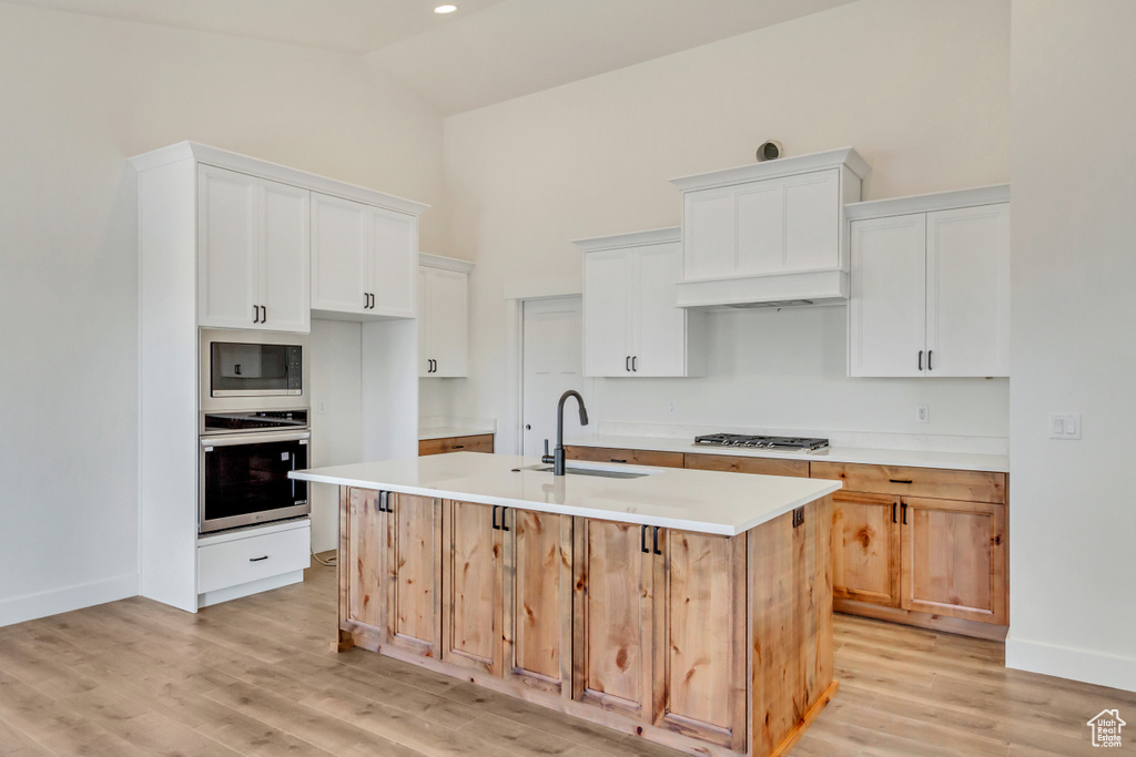 Kitchen featuring sink, light hardwood / wood-style flooring, a kitchen island with sink, white cabinetry, and stainless steel appliances