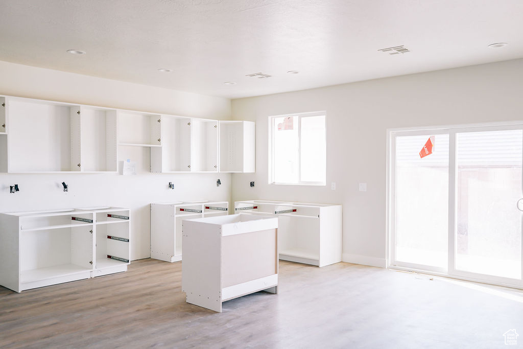 Kitchen with light hardwood / wood-style floors, a center island with sink, and white cabinetry