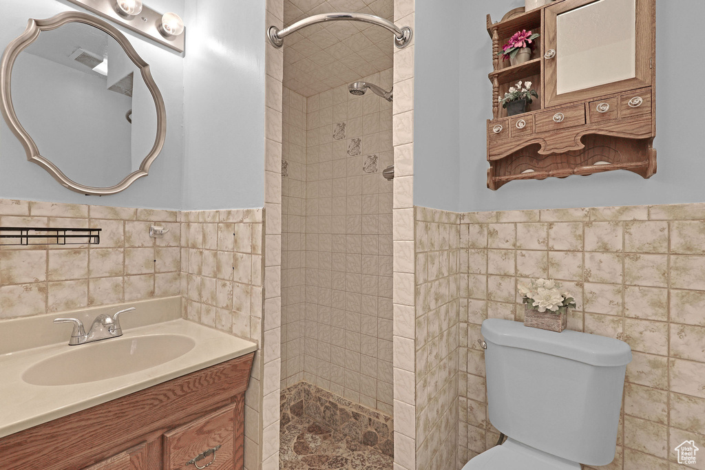 Bathroom with tile walls, vanity, a tile shower, and toilet