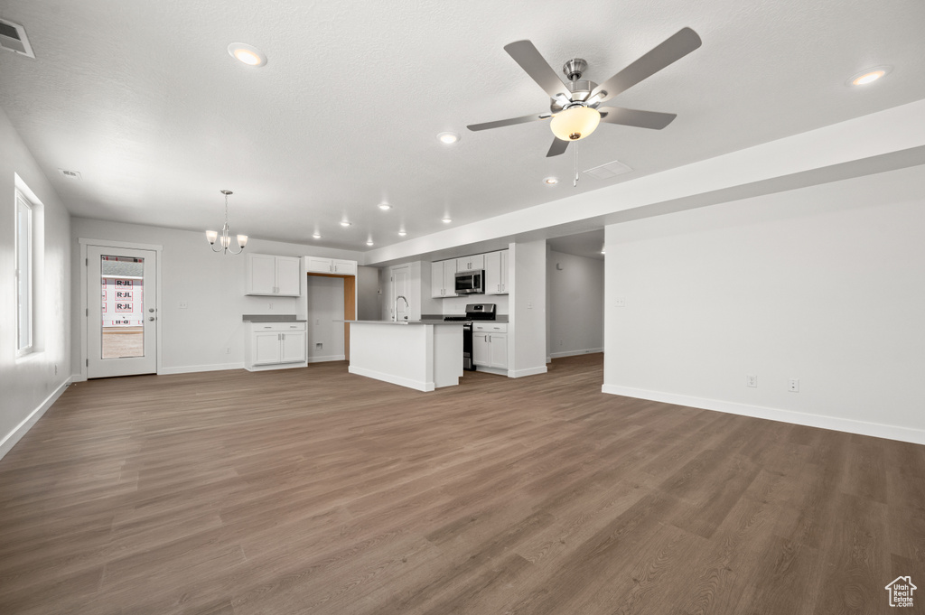 Unfurnished living room with wood-type flooring, ceiling fan with notable chandelier, and sink