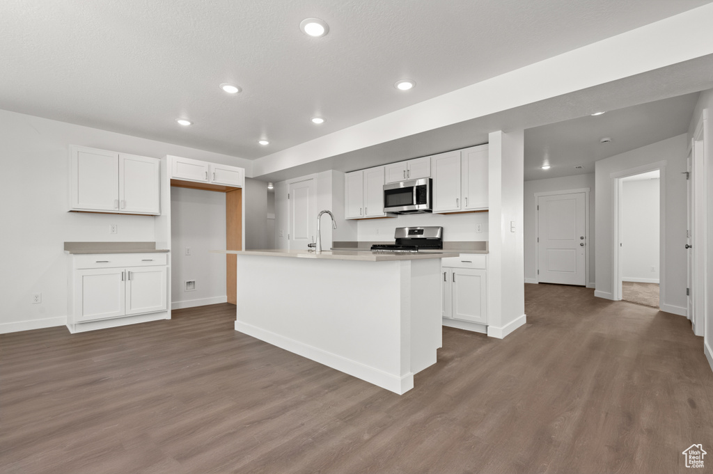 Kitchen with an island with sink, sink, white cabinetry, appliances with stainless steel finishes, and dark hardwood / wood-style floors