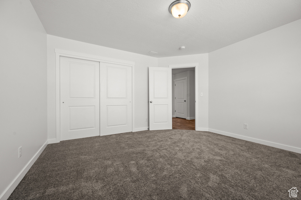 Unfurnished bedroom featuring a closet and dark carpet