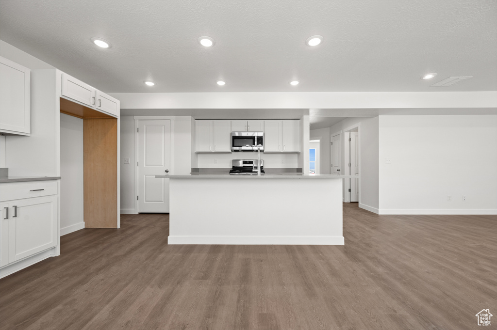 Kitchen with white cabinets, hardwood / wood-style flooring, appliances with stainless steel finishes, a center island with sink, and a textured ceiling