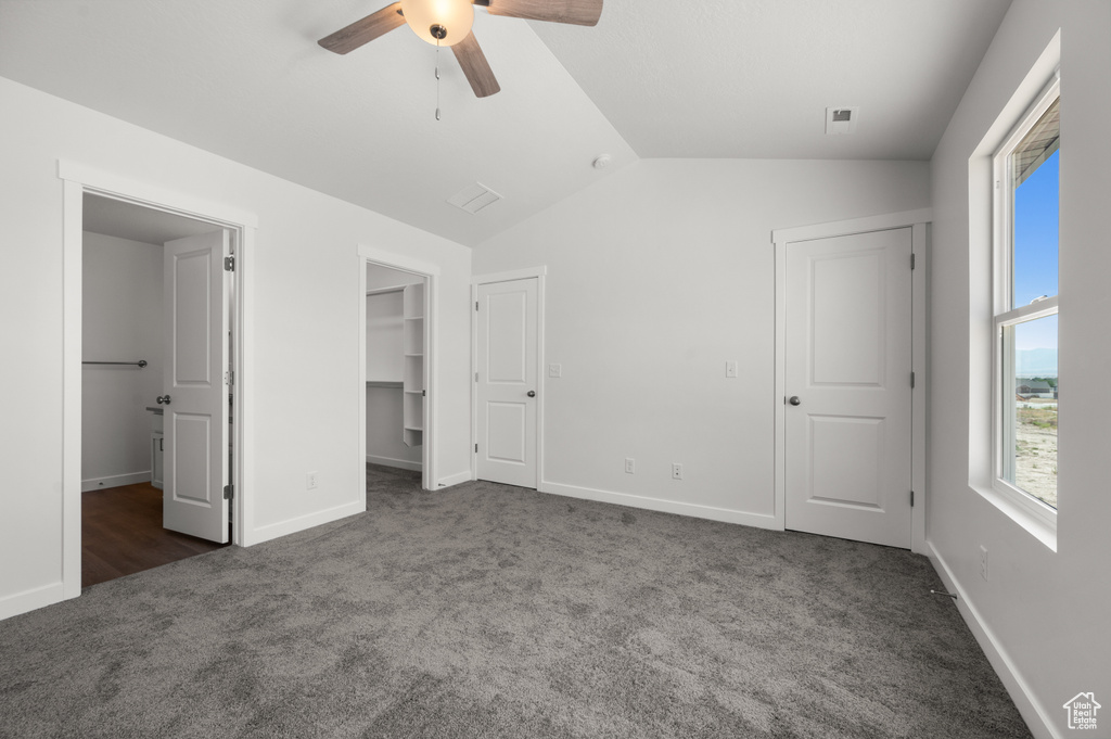 Unfurnished bedroom with ceiling fan, lofted ceiling, a walk in closet, a closet, and dark colored carpet