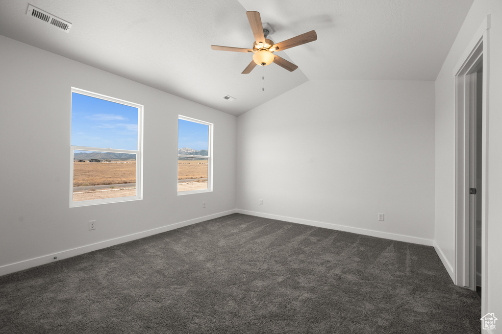 Unfurnished bedroom with dark carpet, vaulted ceiling, and ceiling fan