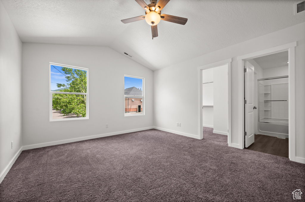 Unfurnished bedroom featuring lofted ceiling, ceiling fan, connected bathroom, dark carpet, and a walk in closet