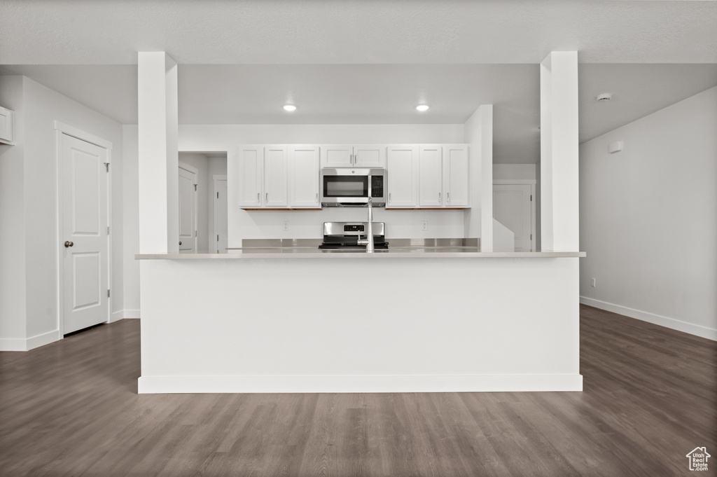 Kitchen with an island with sink, appliances with stainless steel finishes, dark hardwood / wood-style flooring, and white cabinetry