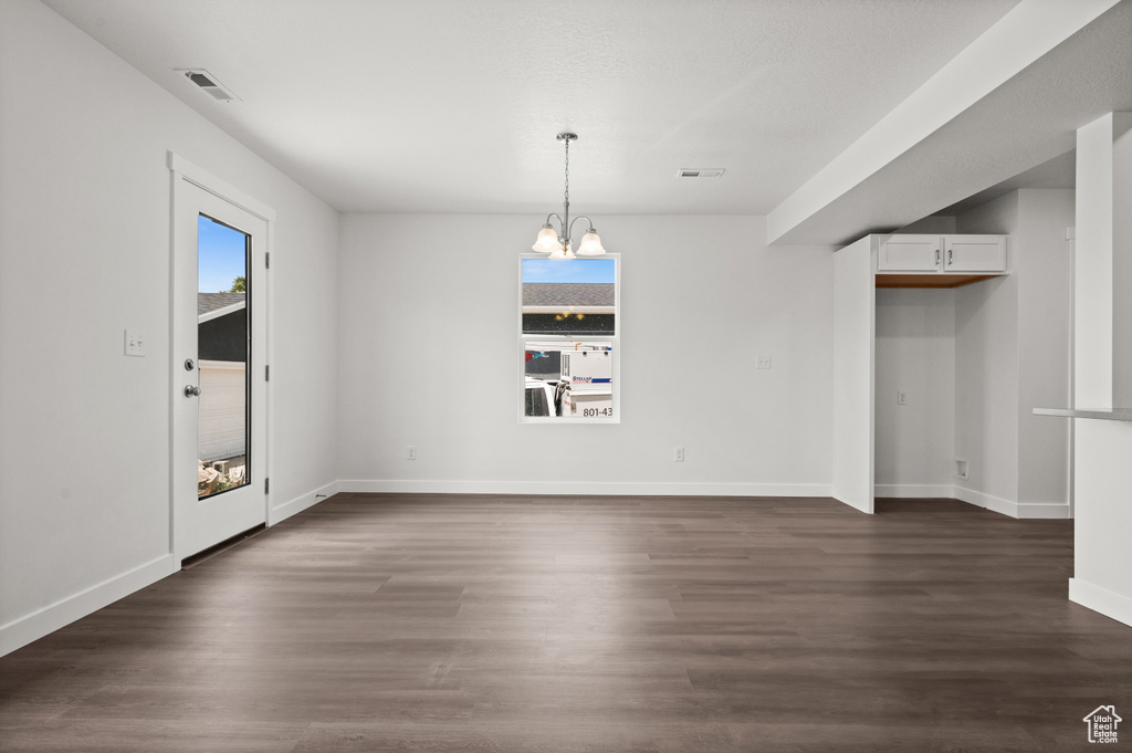 Empty room with an inviting chandelier and dark hardwood / wood-style flooring