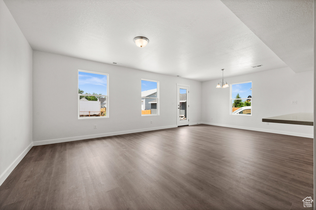 Spare room with a notable chandelier, dark wood-type flooring, and a textured ceiling