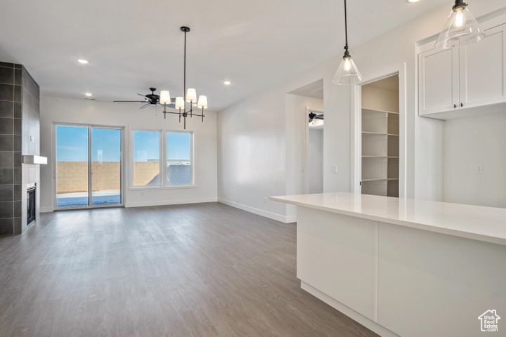 Unfurnished living room with ceiling fan with notable chandelier, dark hardwood / wood-style floors, and a tiled fireplace