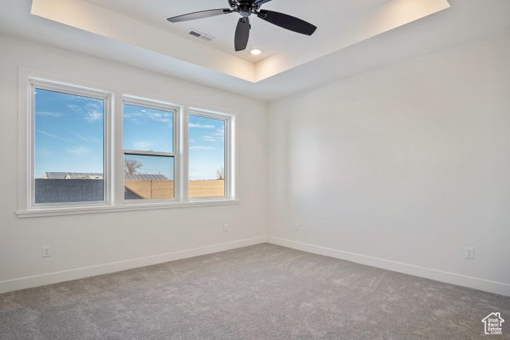 Carpeted empty room with ceiling fan and a tray ceiling