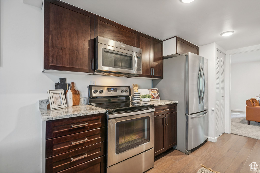 Kitchen with light stone counters, stainless steel appliances, dark brown cabinets, and light hardwood / wood-style flooring