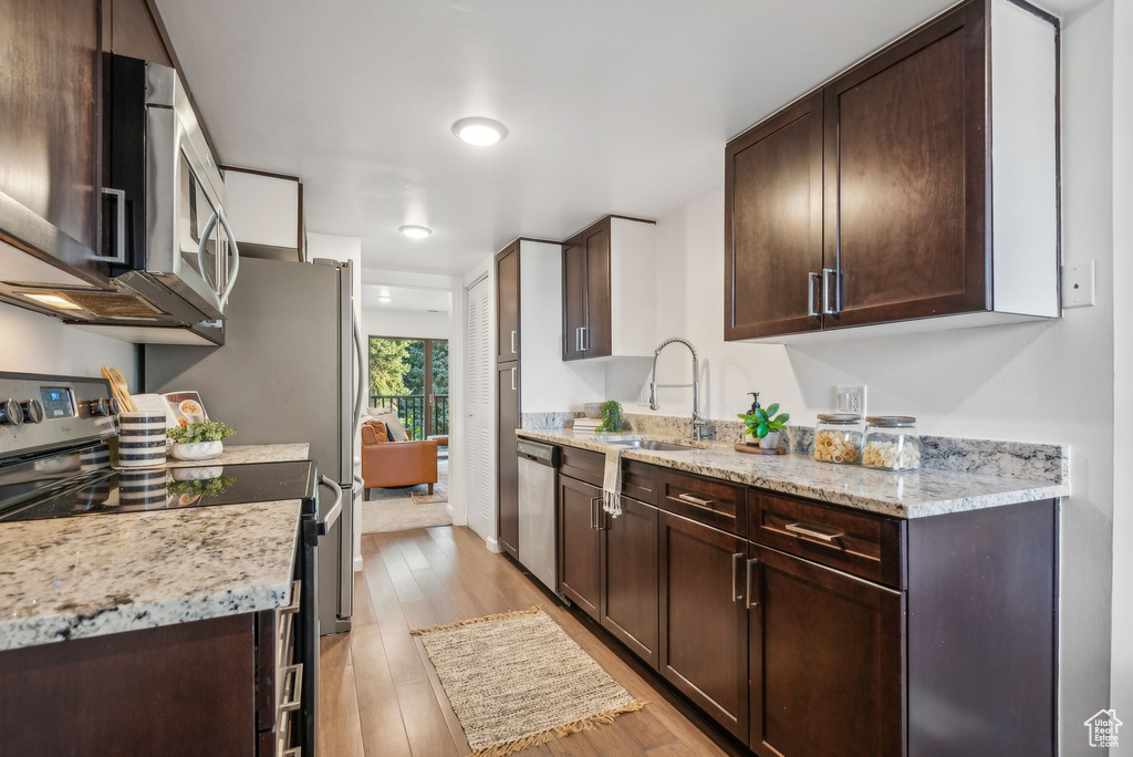 Kitchen with appliances with stainless steel finishes, light hardwood / wood-style flooring, light stone countertops, and dark brown cabinets